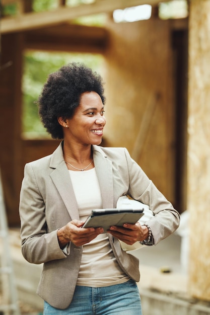 Photo d'une femme architecte africaine utilisant une tablette numérique et vérifiant le chantier de construction d'une nouvelle maison en bois.