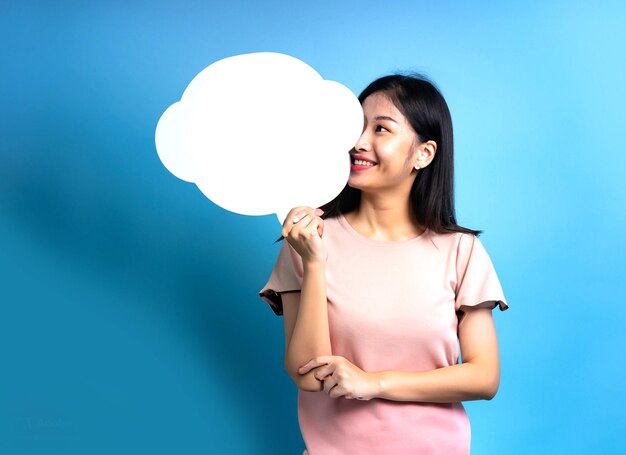 photo d'une femme asiatique heureuse souriante tenant une bulle de discours vide sur fond bleu