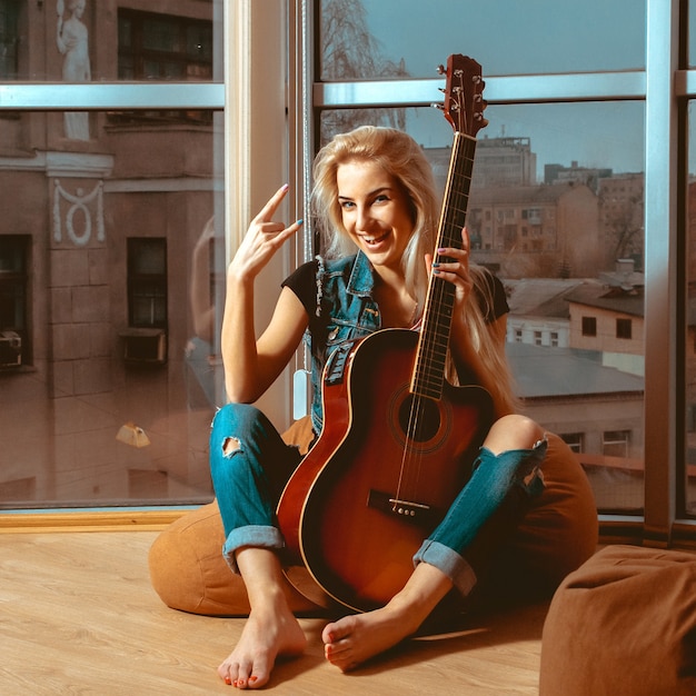 Photo d'une femme blonde amusante avec guitare et beau sourire. Fille avec guitare. Femme jouant de la guitare. loisir avec guitare.