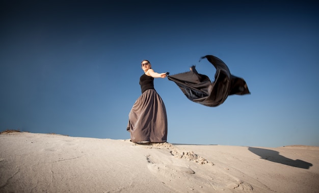 Photo de femme avec un drap noir marchant sur des dunes de sable