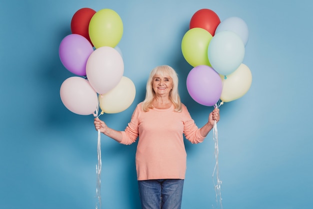 Photo de femme drôle tenir de nombreux ballons à air en pull rose sur fond bleu