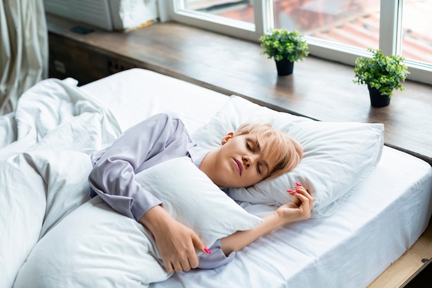 Photo d'une femme endormie, elle se couche sous les couvertures et serre l'oreiller dans ses bras