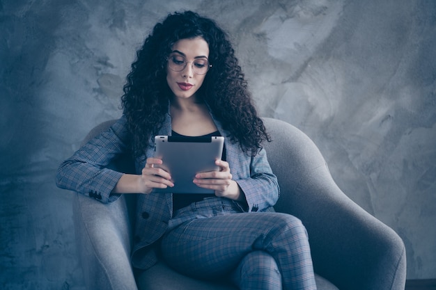 Photo de femme gestionnaire assis dans une chaise utiliser tablet isolé sur fond de mur de béton