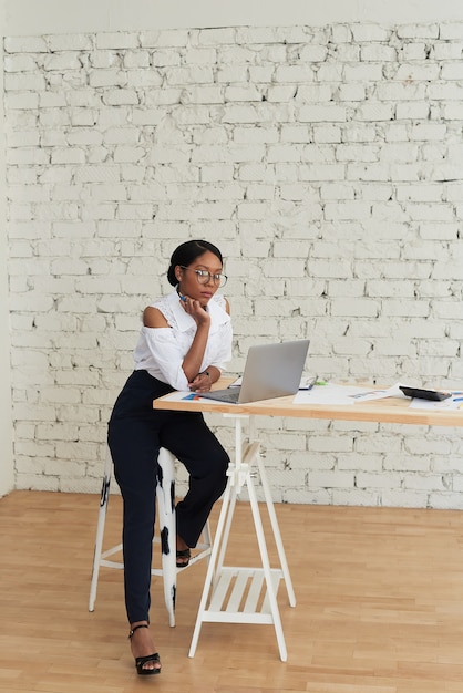 Photo d'une femme métisse joyeuse et joyeuse en chemise blanche tenant une formation ou une conférence à l'aide d'un ordinateur portable.