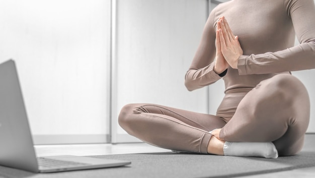 Photo d'une femme pratiquant une formation de yoga en ligne à la maison avec un ordinateur portable.