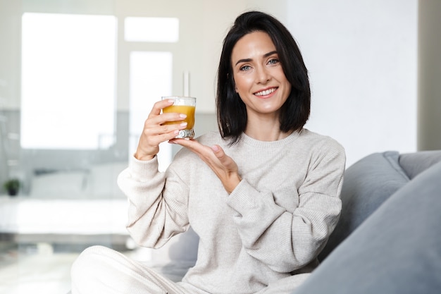 Photo de femme de race blanche 30 s buvant du jus d'orange, assis sur un canapé dans une pièce lumineuse