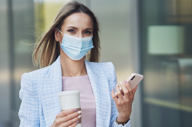 Photo d'une femme séduisante adulte portant un masque avec un smartphone marchant dans la ville