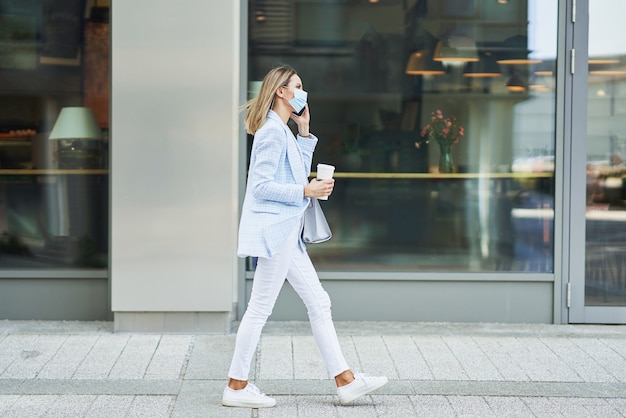 Photo d'une femme séduisante adulte portant un masque avec un smartphone marchant dans la ville