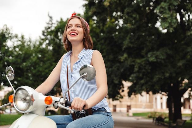 Photo de femme souriante hipster assis sur un scooter et à l'extérieur