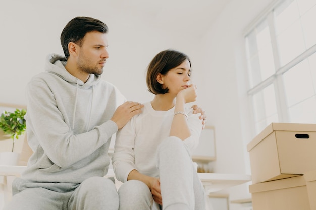 Photo d'une femme triste se plaint des problèmes que l'homme calme embrasse sa femme fatiguée après avoir apporté de nombreuses boîtes avec des choses à leur nouvelle maison porter des vêtements décontractés étant stressant Concept de problèmes familiaux