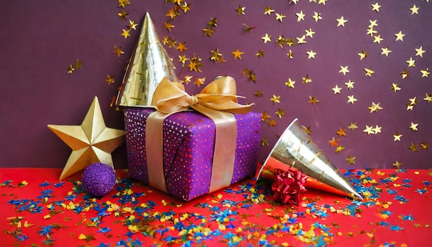 Photo photo festive étoiles dorées et violettes de confetti et un cadeau de capuchon d'anniversaire sur un fond rouge