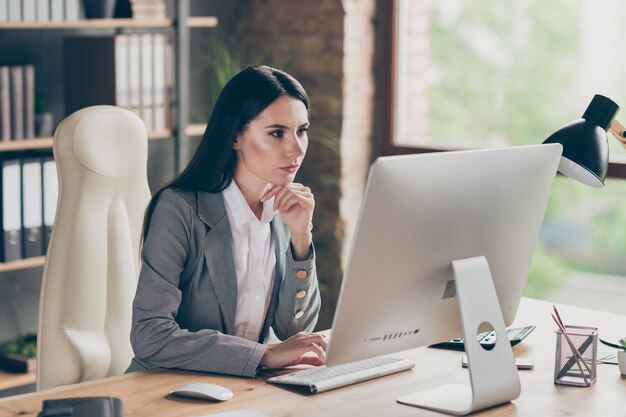 Photo d'une fille au col à l'esprit pensif s'asseoir à table travailler à distance sur un écran d'ordinateur pc analyser le projet de marché de l'entreprise d'emploi porter une veste de blazer sur le lieu de travail bureau moderne