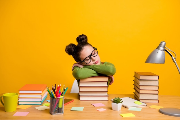 Photo de fille de l'école s'asseoir la tête de bureau sur le livre se détendre isolé sur fond jaune