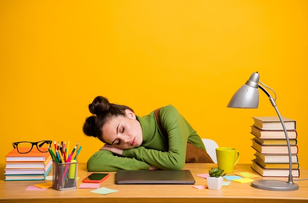 Photo d'une fille endormie s'asseoir au bureau avec un ordinateur portable isolé sur fond jaune