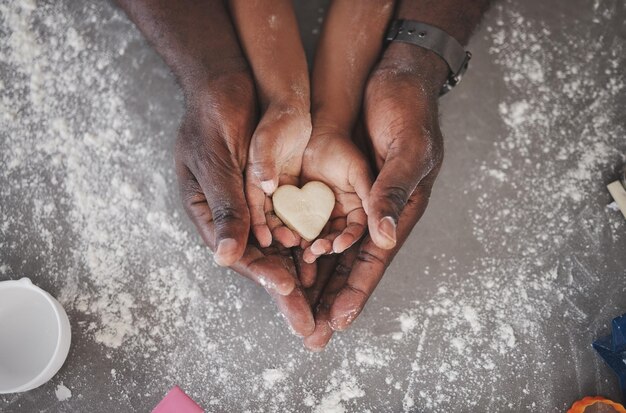 Photo d'une fille méconnaissable et de son père tenant un cookie en forme de coeur dans la cuisine à la maison