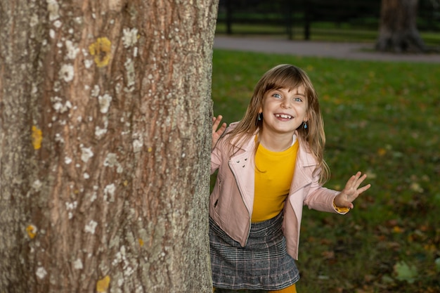 Photo de fille mignonne drôle sans dents jouant à cache-cache dans le parc de l'automne.