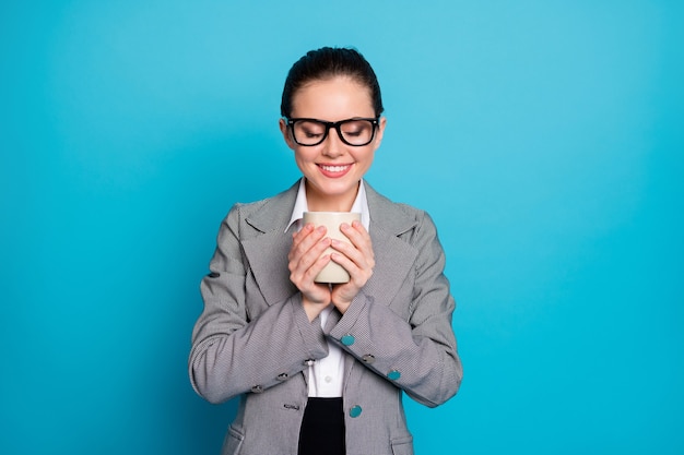 Photo de fille positive tenir mug boisson odeur porter costume blazer gris isolé sur fond de couleur bleu