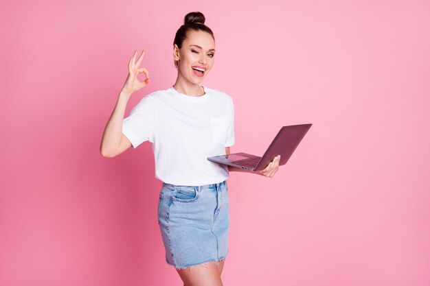 Photo d'une fille positive travaillant à distance sur un ordinateur portable recommande de montrer un signe porter un t-shirt blanc en jean denim