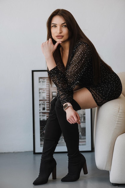 Photo d'une fille en vêtements sombres et chaussures hautes sur une chaise blanche