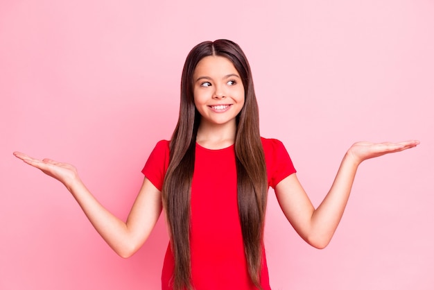Photo d'une fillette tenir la main regarder un espace vide pour les annonces porter un t-shirt rouge isolé sur fond de couleur pastel