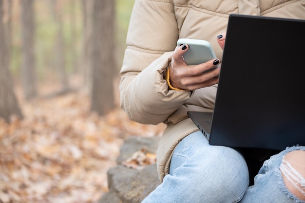 Photo frontale d'une femme méconnaissable travaillant avec un ordinateur portable et un téléphone portable au milieu de la forêt, avec espace de copie