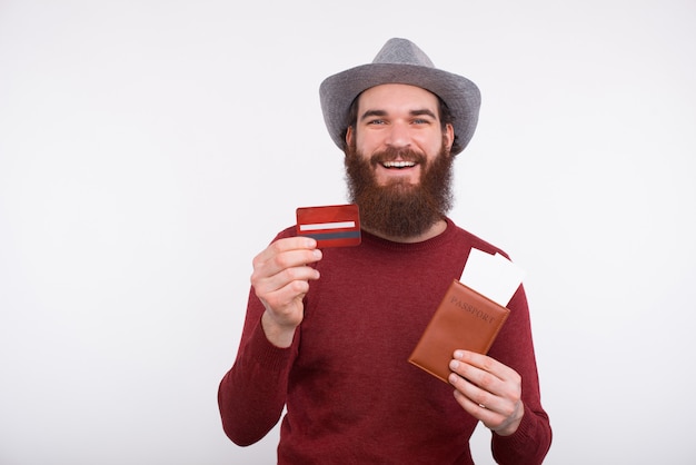 Photo de gai jeune homme barbu tenant des billets de passeport et une carte de crédit