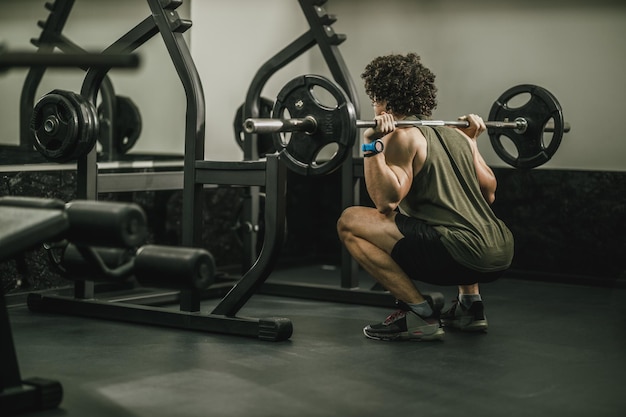 Photo d'un gars musclé en vêtements de sport qui s'entraîne dur dans une salle de sport. Il fait des exercices de squat avec des haltères.