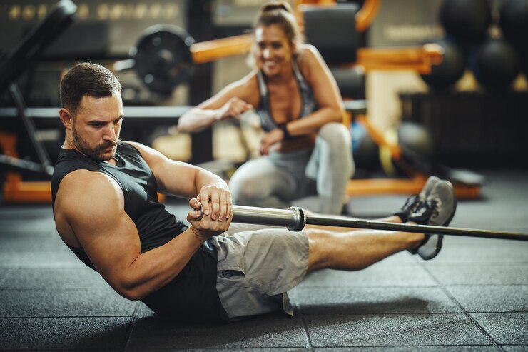 Photo d'un gars musclé en vêtements de sport qui s'entraîne avec des haltères dans la salle de sport d'entraînement croisé. Il gonfle les muscles abdominaux avec un poids lourd.