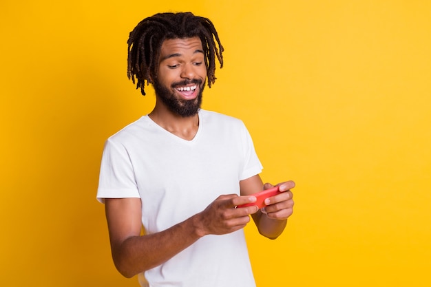 Photo d'un gars à la peau sombre et funky tenir le téléphone en jouant à un nouveau jeu vidéo d'arcade isolé sur fond de couleur jaune