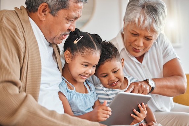 Photo de grands-parents se liant avec leurs petits-enfants et utilisant une tablette numérique sur un canapé à la maison