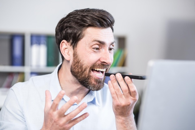 La photo en gros Employé de bureau en colère et agacé Il parle sur son téléphone portable crie Assis à un bureau d'ordinateur