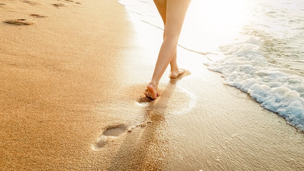 Photo en gros plan d'une belle jeune femme aux pieds nus marchant dans les vagues calmes et chaudes de la mer contre un coucher de soleil incroyable