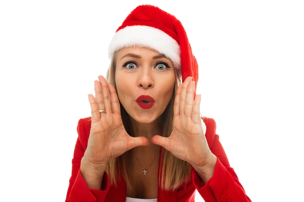 Photo en gros plan d'une belle jeune femme en bonnet de Noel, tenant les mains autour de la bouche et faisant des grimaces