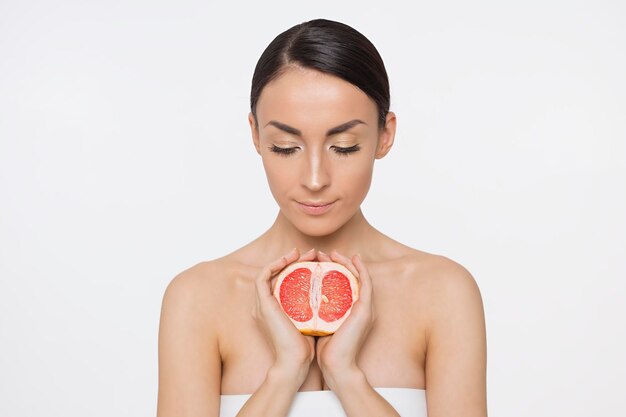 La photo en gros plan d'une belle jeune femme souriante avec un demi-pamplemousse juteux sur fond blanc