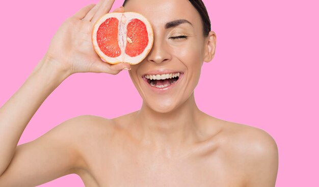 La photo en gros plan d'une belle jeune femme souriante avec un demi-pamplemousse juteux sur fond blanc