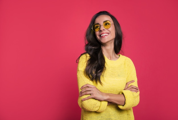 Photo en gros plan d'une belle jeune femme en tenue jaune et lunettes de soleil, qui rit les yeux fermés et pose