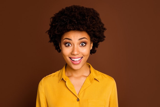 Photo gros plan de la belle jolie peau foncée dame bouclée bouche ouverte expression faciale joyeuse écouter incroyable bonnes nouvelles porter chemise jaune couleur marron isolé