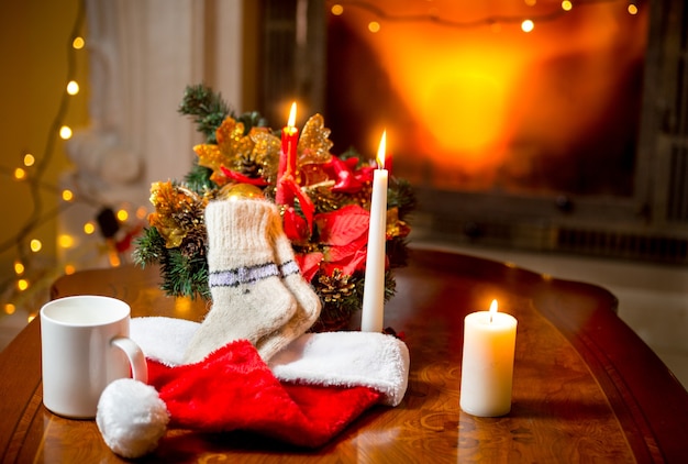 Photo gros plan de bougies allumées, de chaussettes en laine et de bonnet de Noel allongé sur une table contre une cheminée