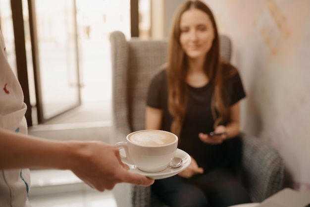 Une photo en gros plan d'un café au lait qu'une femme barista tend à une fille dans un café.