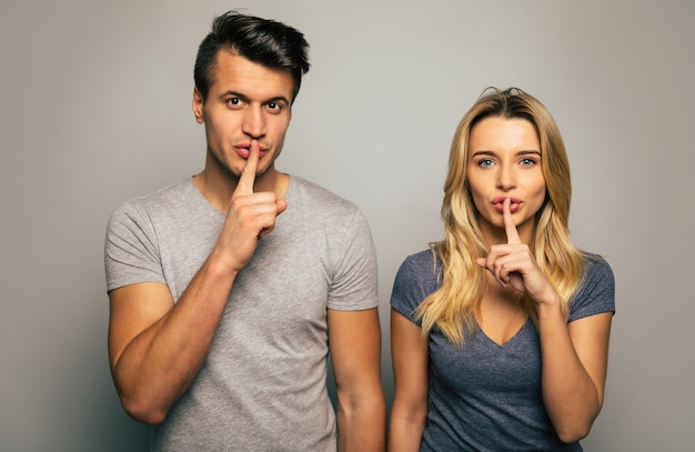 Photo en gros plan d'un couple énigmatique, qui pose devant, en appuyant ses index sur ses lèvres et en regardant dans l'appareil photo.