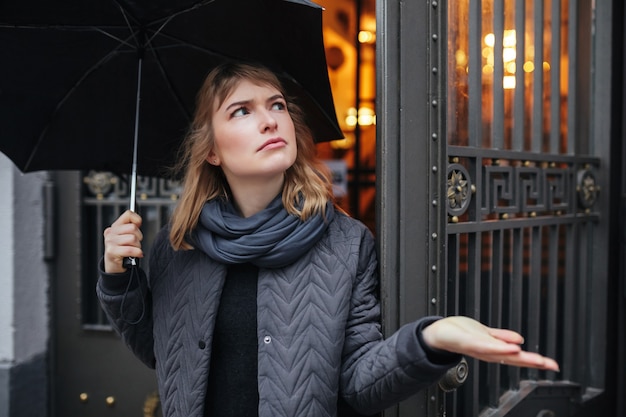 La photo en gros plan d'une dame triste debout sur la rue avec un parapluie noir