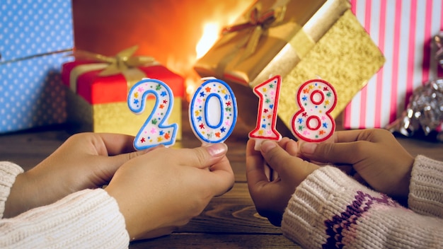 Photo en gros plan de deux filles tenant des numéros de 2018 à côté d'une cheminée en feu et de cadeaux de Noël colorés