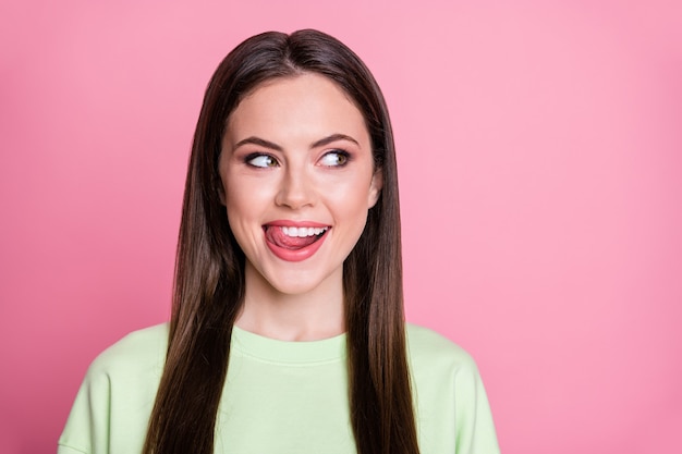 Photo en gros plan d'une drôle de dame séduisante longue coiffure léchant la langue des lèvres de fille voir un délicieux dessert regarder côté espace vide porter un sweat-shirt vert décontracté pull isolé sur fond de couleur rose