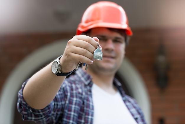 Photo gros plan du travailleur de la construction tenant les clés de la nouvelle maison à la main