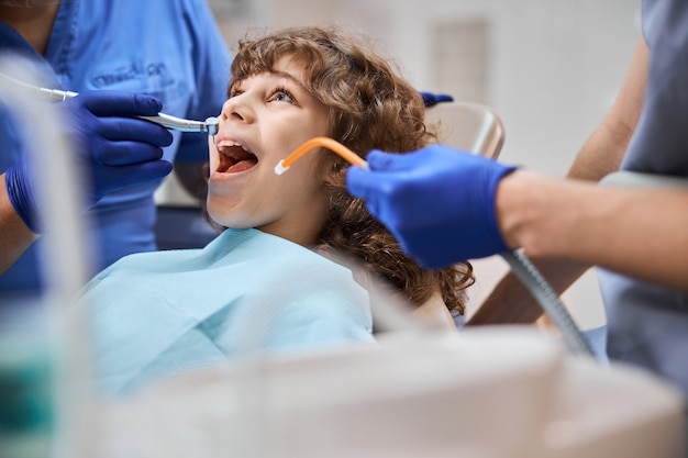 Photo en gros plan d'un enfant patient recevant un traitement dentaire d'un dentiste avec une fraise dentaire