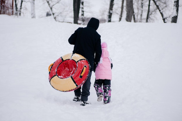 Photo en gros plan d'un enfant et d'un père avec un traîneau qui monte une colline pour glisser dans la neige en forêt Fond étonnant plein de couleur blanche et de neige