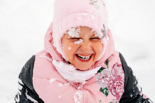 Photo en gros plan d'une enfant russe souriante avec des dents avec le visage couvert de neige, les yeux fermés ...