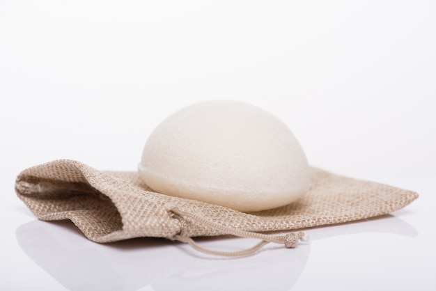 Photo en gros plan d'une éponge de konjac blanche sans additifs allongée sur un petit sac d'emballage artisanal isolé sur fond blanc