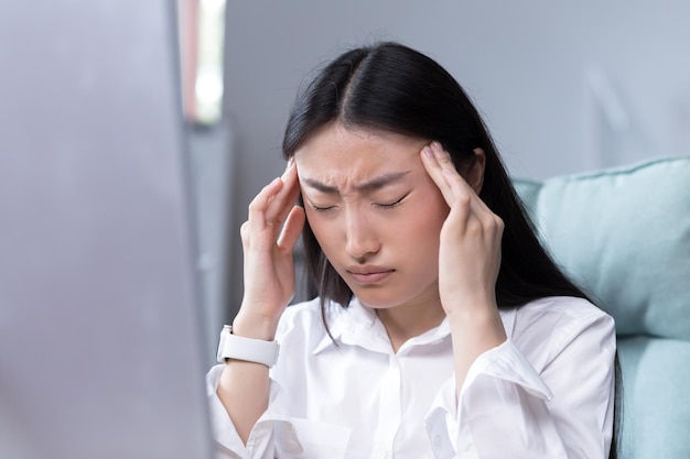 Photo en gros plan d'une femme d'affaires fatiguée au bureau ouvrière asiatique tenant les mains sur la tête ayant