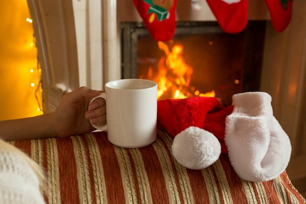 Photo gros plan d'une femme assise avec une tasse de thé sur un canapé à la cheminée